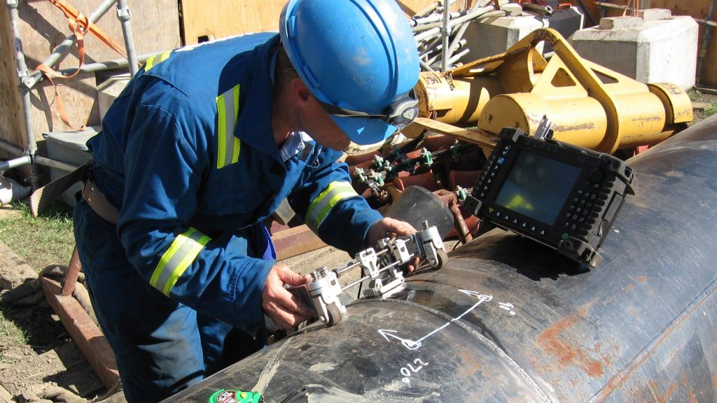 At a construction site, a technician tests a pipeline weld for defects using an ultrasonic phased array instrument.