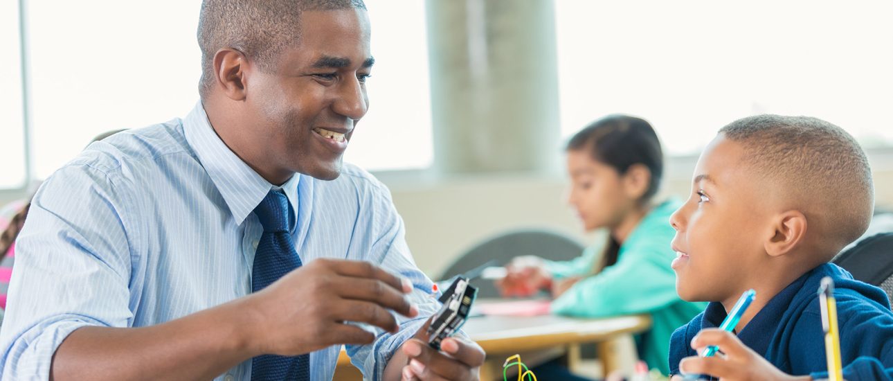 Man is teaching elementary little boy about robotics during school STEM program