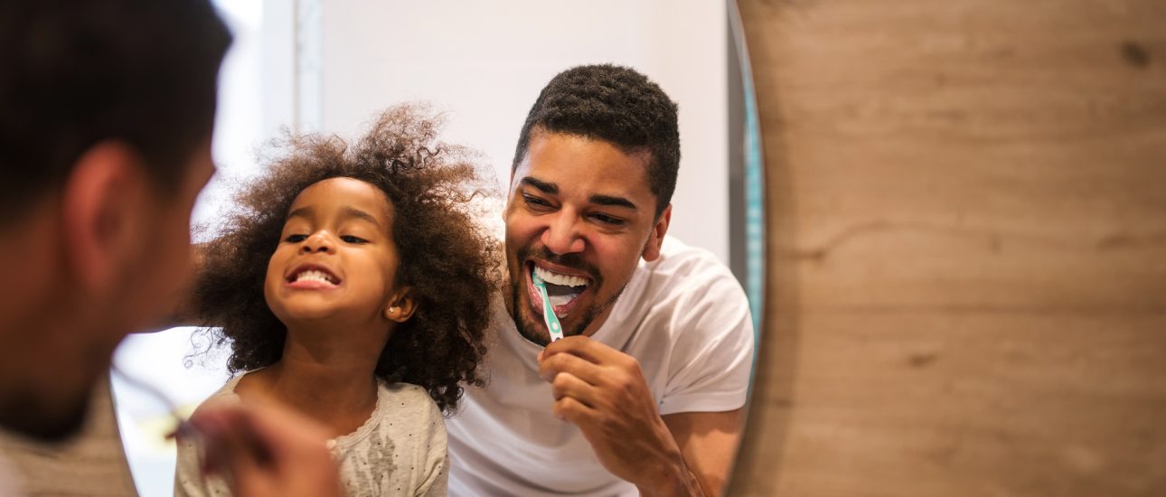 Dad showing daughter how to brush teeth