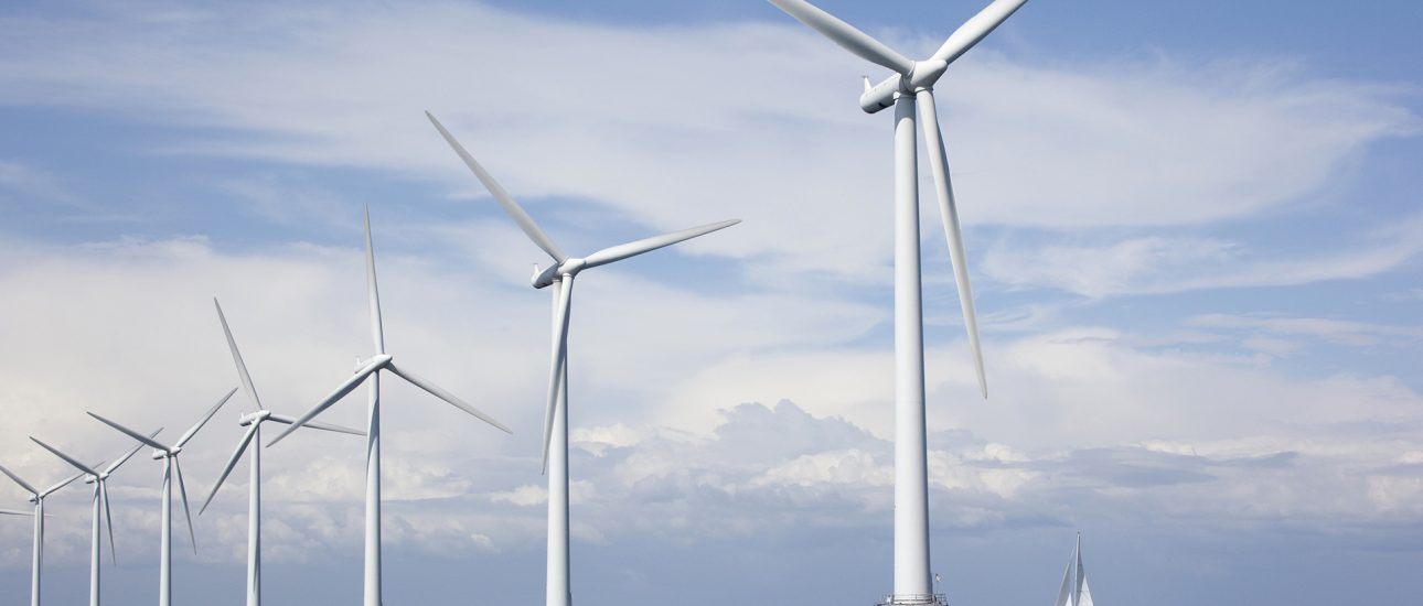 Large white windmills in the sea with a sailboat