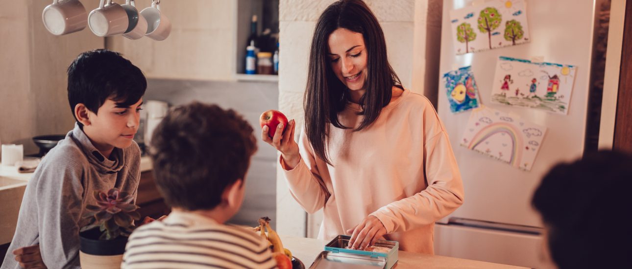 Mother preparing healthy food lunch boxes for children in kitchen