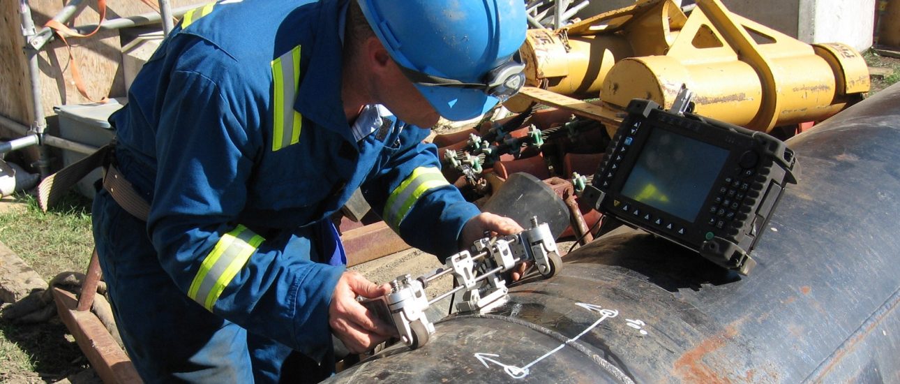 At a construction site, a technician tests a pipeline weld for defects using an ultrasonic phased array instrument.